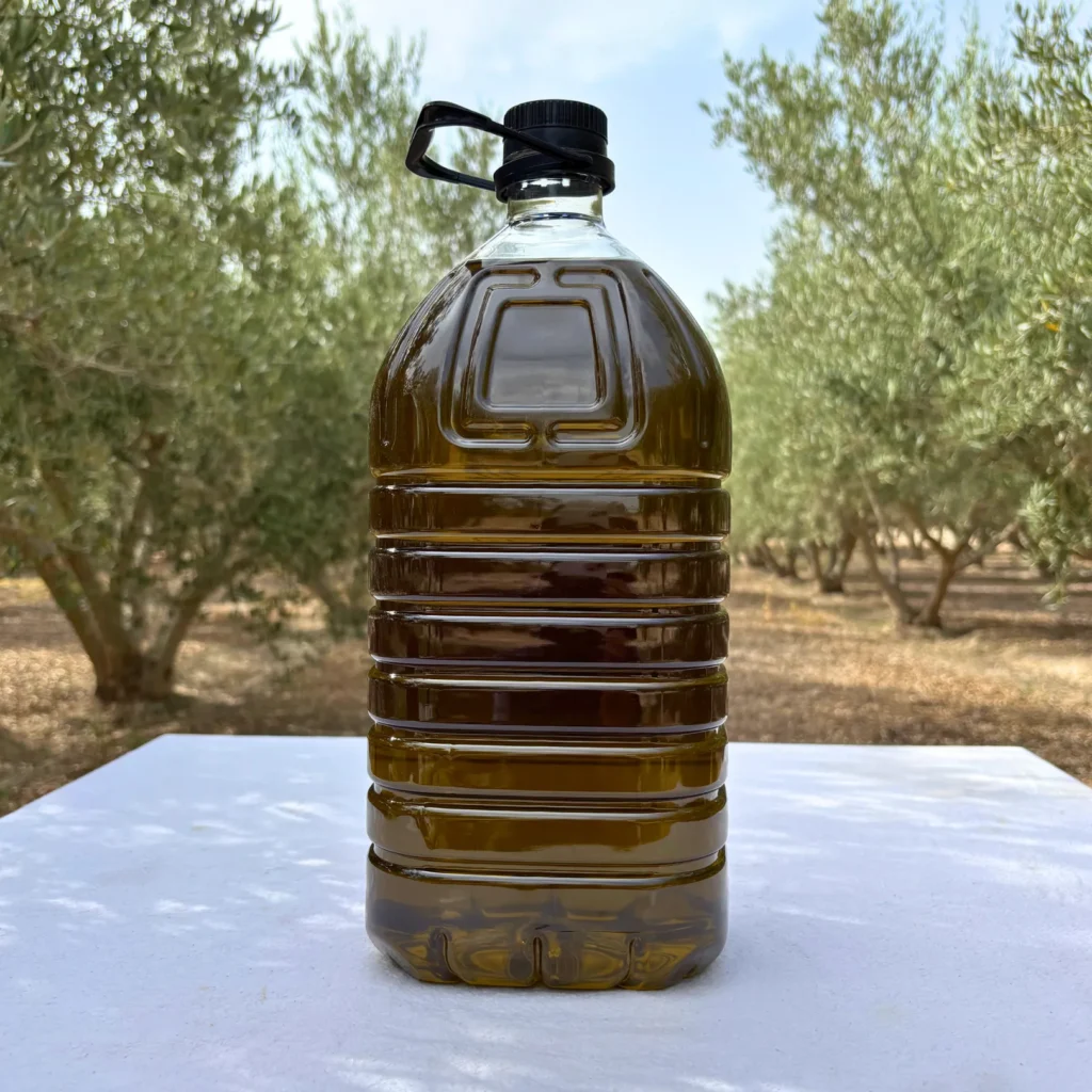 Garrafa de aceite Picual de 5 litros mostrando el color del aceite, en el olivar